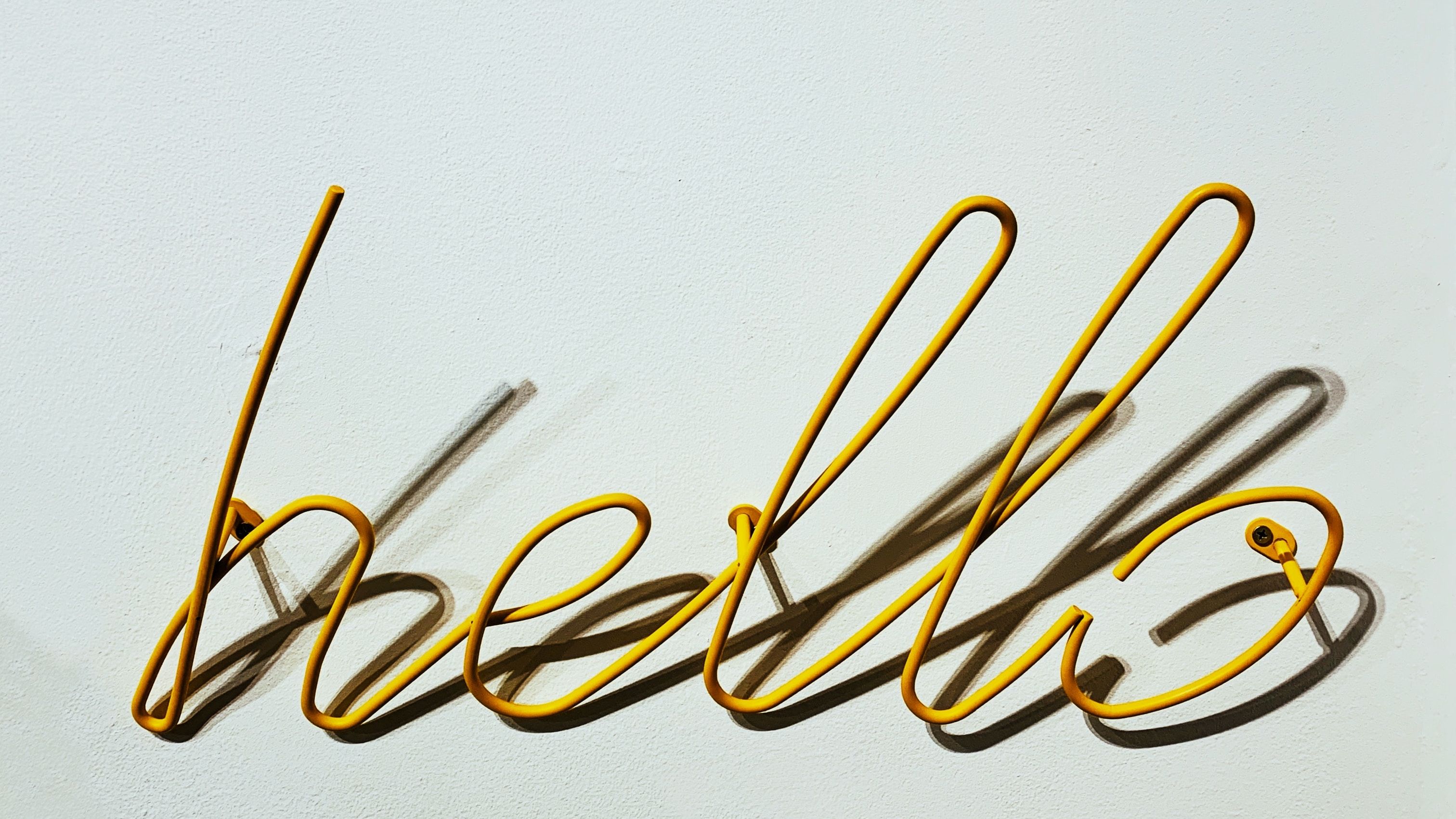 An orange wire sculpture of the word 'hello' in cursive.